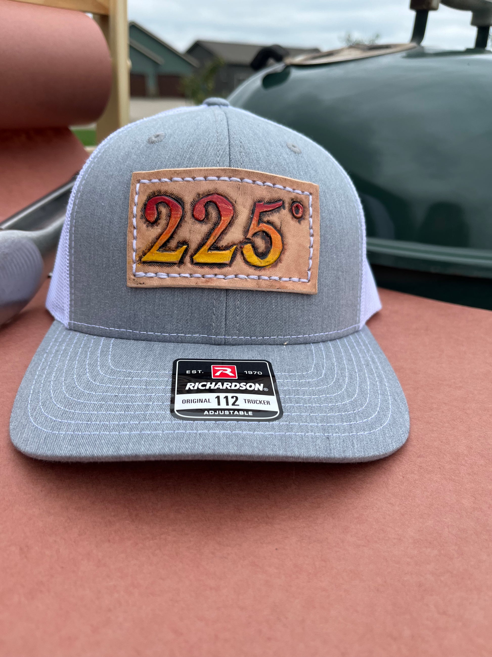 Gray and white richardson 112 trucker hat with a tooled leather patch in the center. Patch has 225 degrees tooled onto it and painted with an ombre of heat starting with a yellow bottom and moving up to orange and red.